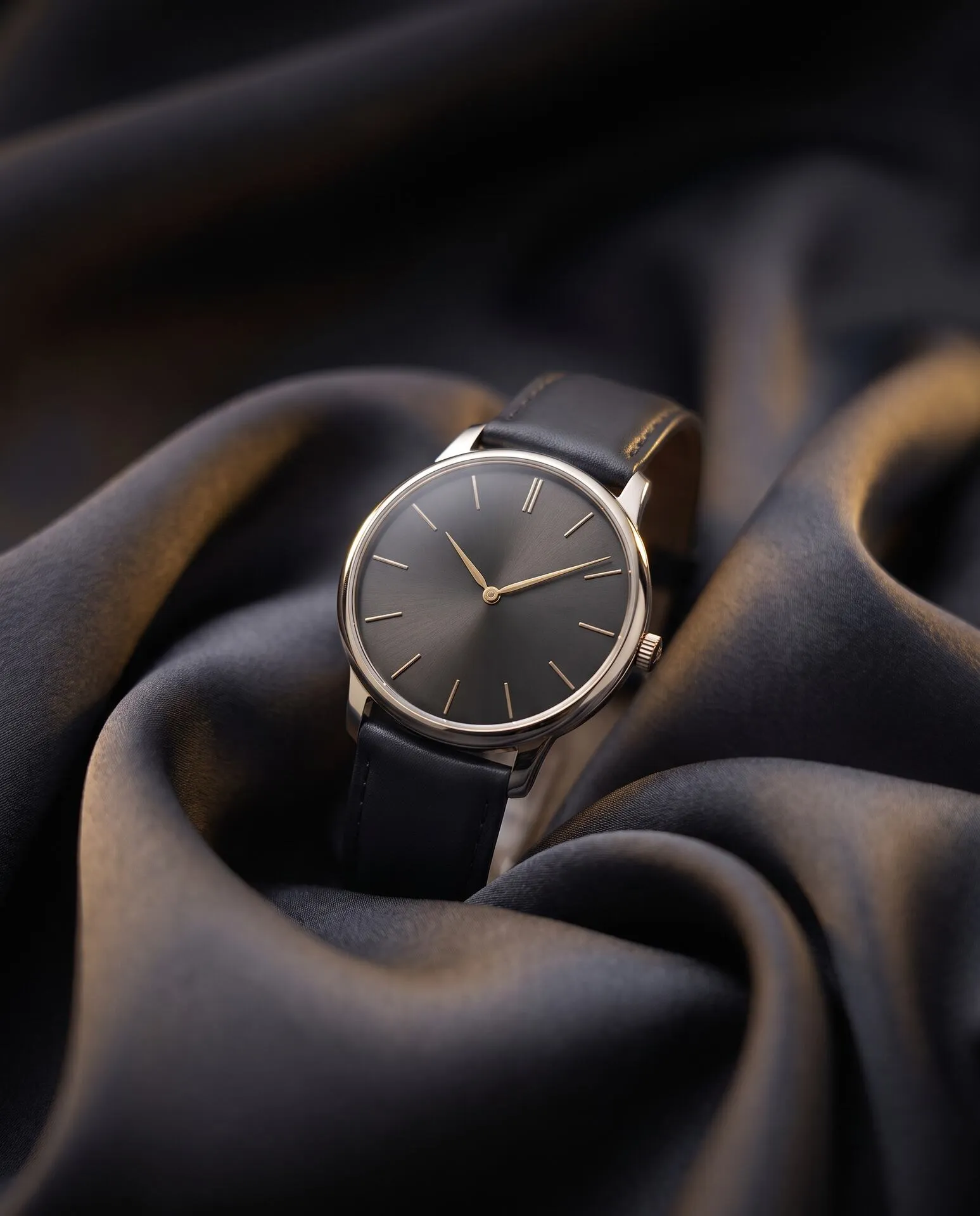 White-gold dress watch with charcoal sunburst dial resting on charcoal silk